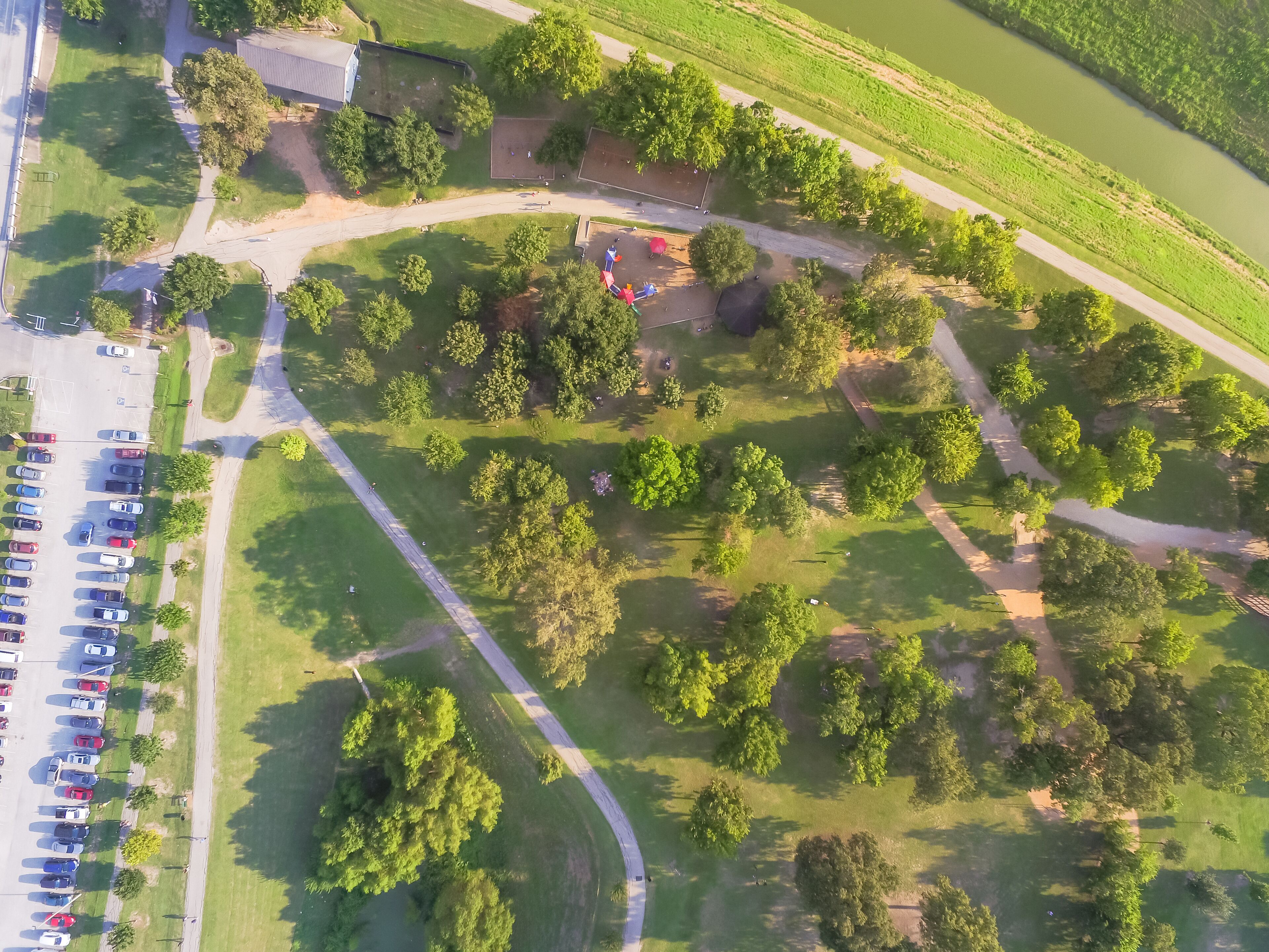 Aerial view busy parking lots at trailhead of urban park with playground, pathway in Houston