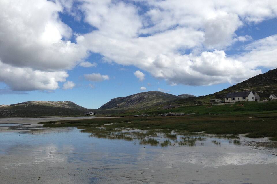A coastal landscape with a calm body of water reflecting the sky and surrounding hills.