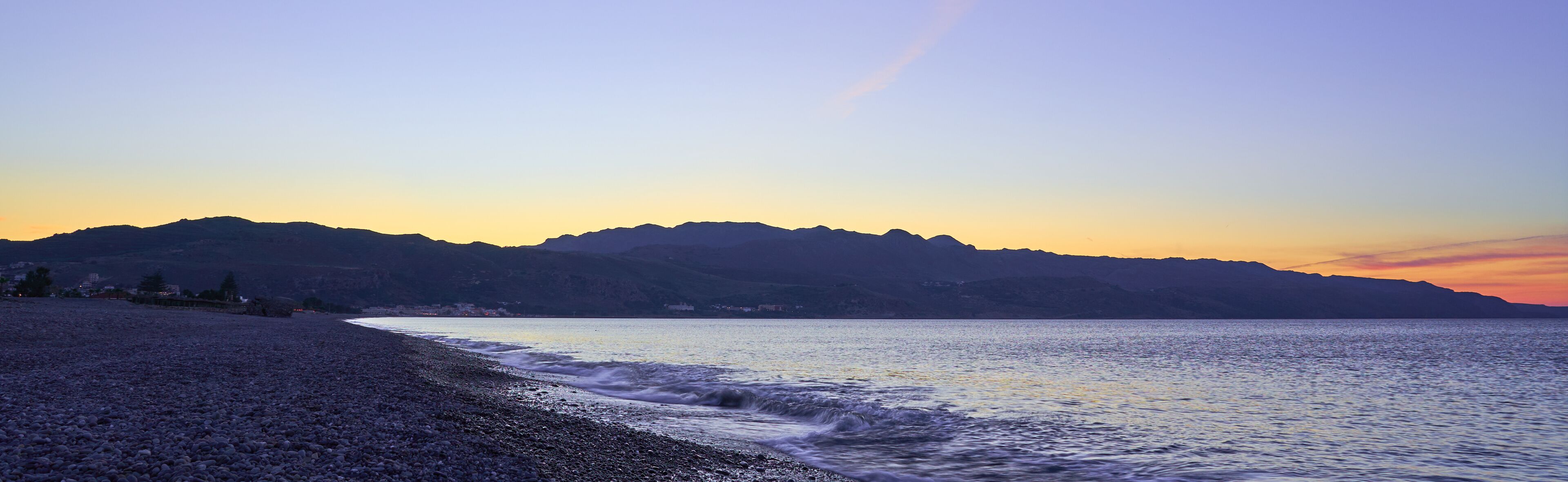 The sunset on the pebble beach with hills on the background, Kolymbari, Crete, Greece.