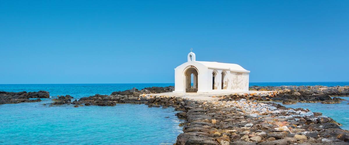 A white church on a rocky shoreline with clear blue water.
