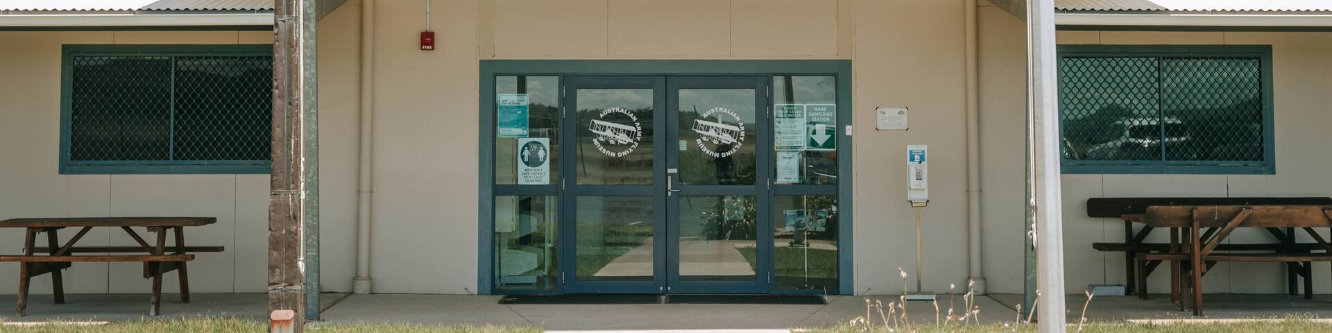 The entrance to the Australian Army Flying Museum with a green sign, glass doors, and a picnic table in the foreground.