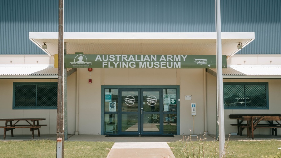 The entrance to the Australian Army Flying Museum with a green sign, glass doors, and a picnic table in the foreground.