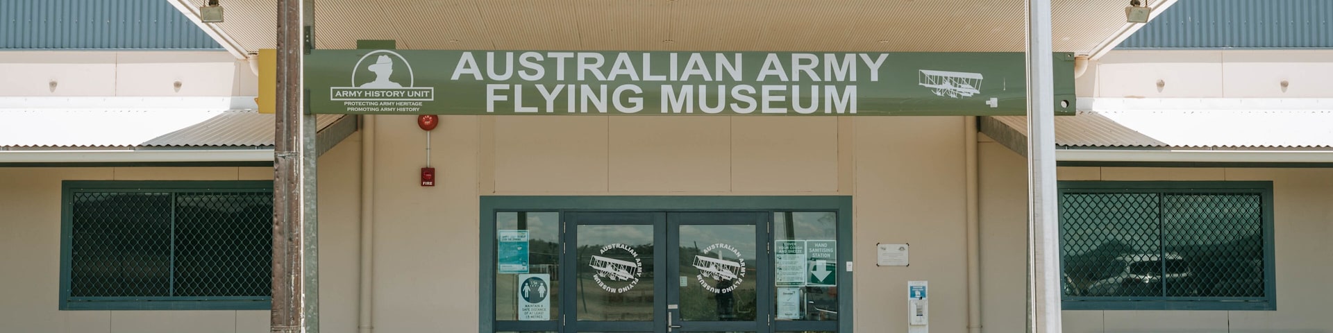 La entrada al Museo del Vuelo del Ejército Australiano, con un letrero verde, puertas de cristal y una mesa de picnic al frente.