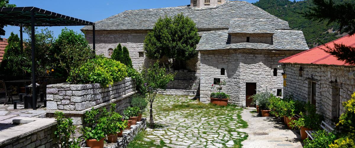 A stone building with a red roof, surrounded by potted plants and a cobblestone path.