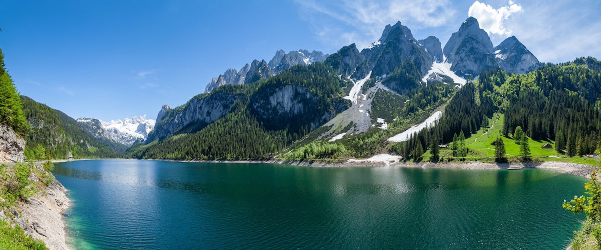 A mountain lake with clear turquoise water, surrounded by rugged mountains and dense forests.