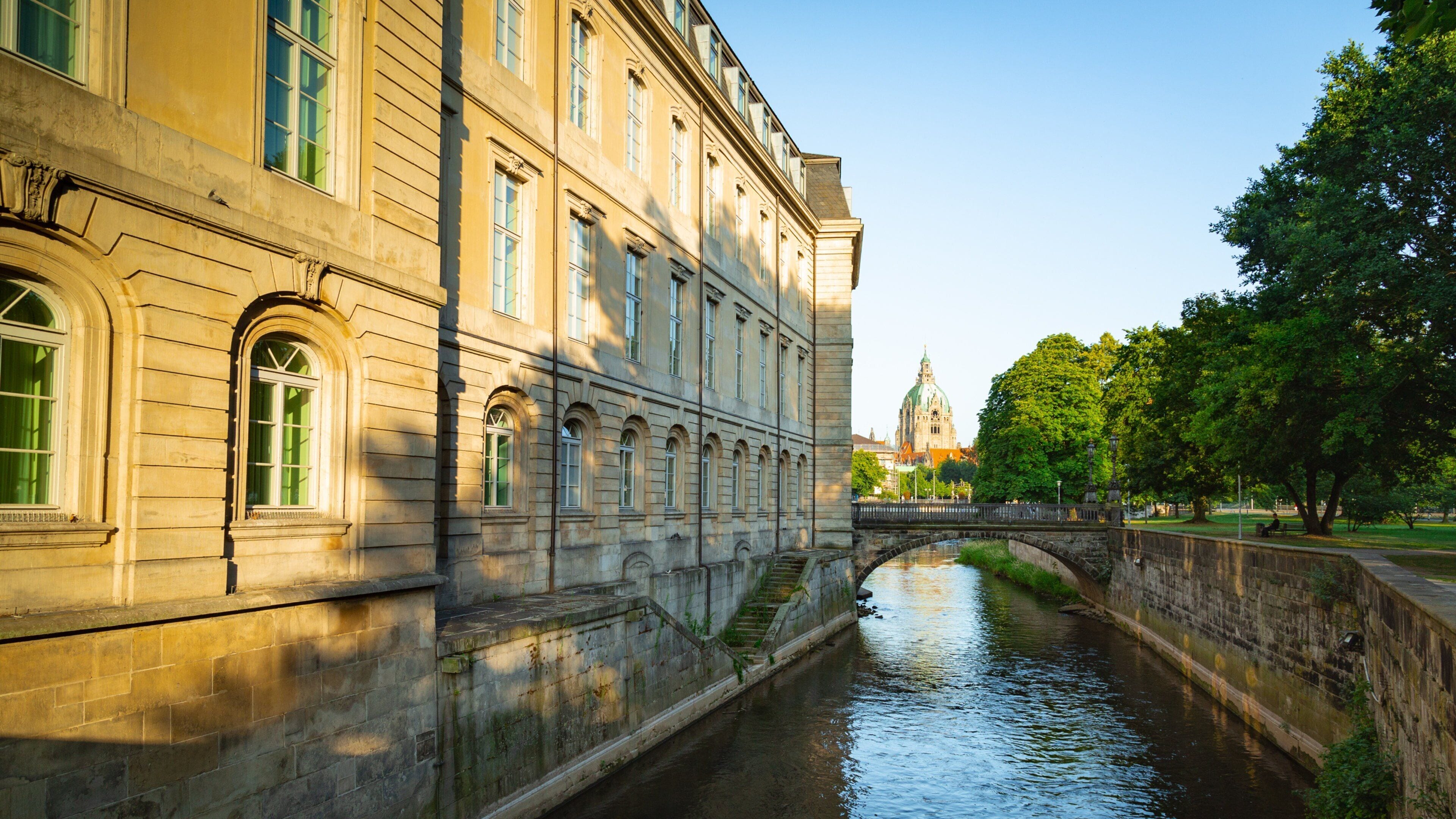 A canal with a stone bridge, a historic building with arched windows, and a distant church tower.