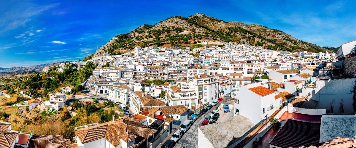 A coastal town with white buildings, terracotta roofs, and a hillside backdrop.