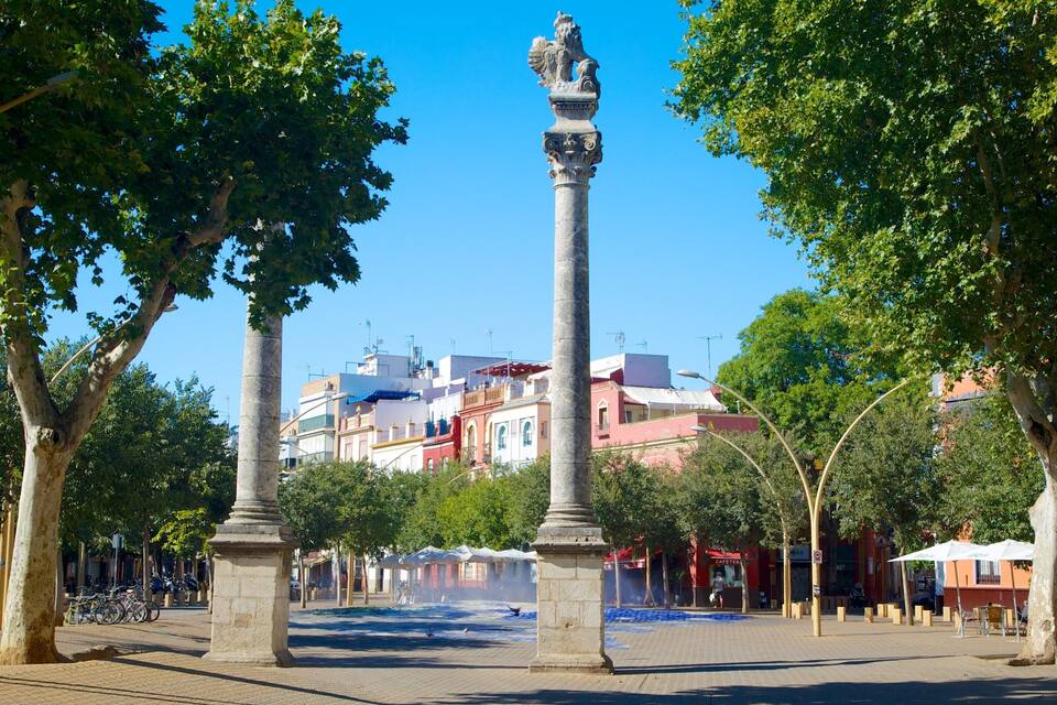 Una plaça amb un monument al centre, rodejada d'arbres i edificis al fons.