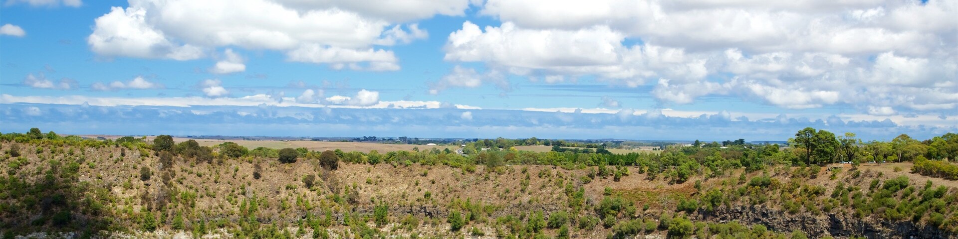 Paisaje costero con mar azul transparente, vegetación verde y una vista distante del horizonte bajo un cielo parcialmente nublado.