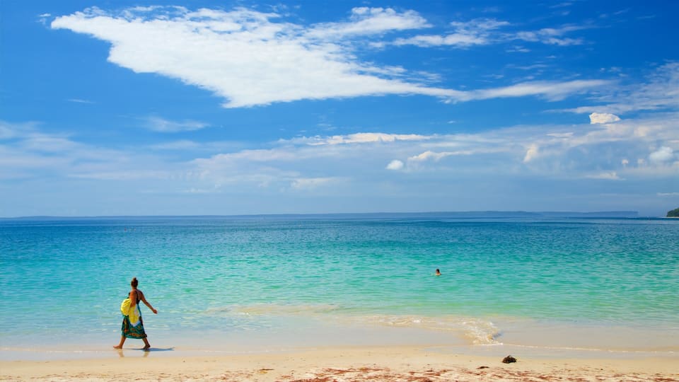 A beach with clear turquoise water, a person in a colorful dress, and a distant shoreline.