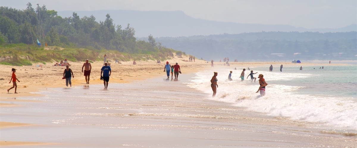 A crowded beach with people walking and playing in the water.