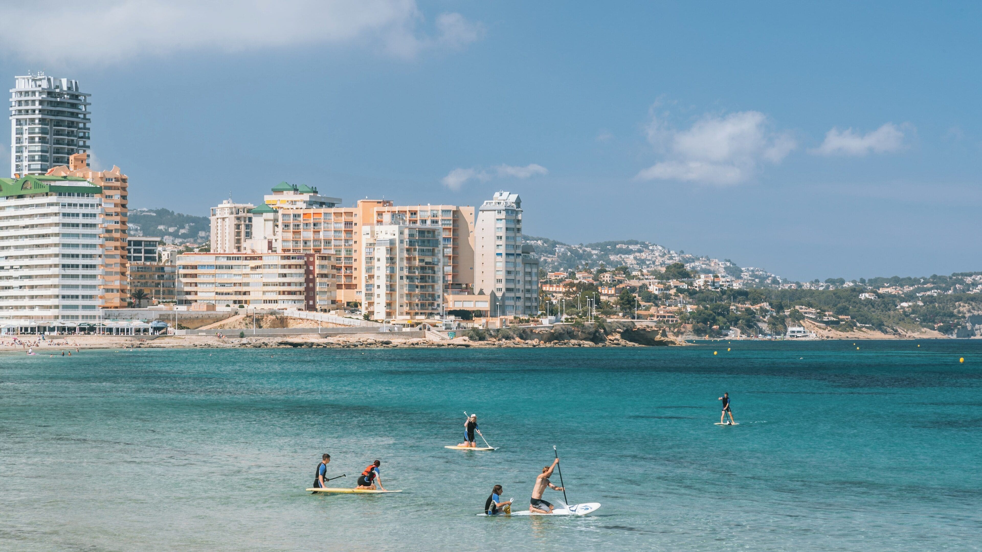 Enjoying water sports at La Fossa Beach, Calpe, Spain on a sunny day with paddleboarders gliding across the clear turquoise waters