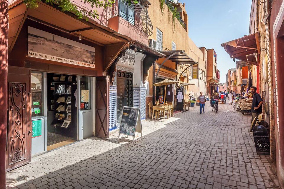 A cobblestone street with shops and a sign that reads "MAISON DE LA PHOTOGRAPHIE DE MARRAKECH."