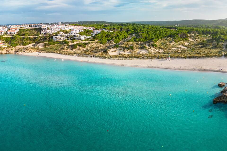 A coastal town with a beach, clear turquoise waters, and surrounding greenery.