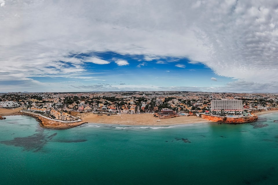 An aerial view of a coastal city with a prominent beach, a large hotel, and a mix of residential and commercial buildings.