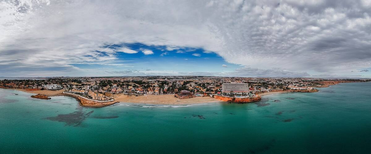 An aerial view of a coastal city with a prominent beach, a large hotel, and a mix of residential and commercial buildings.
