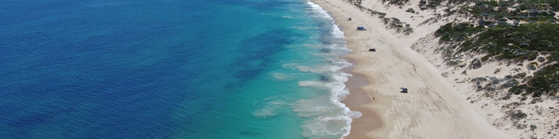 Un paisaje costero con una playa arenosa, aguas azules cristalinas y vegetación escasa.