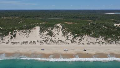 A beach with clear turquoise waters, sandy dunes, and sparse vegetation.