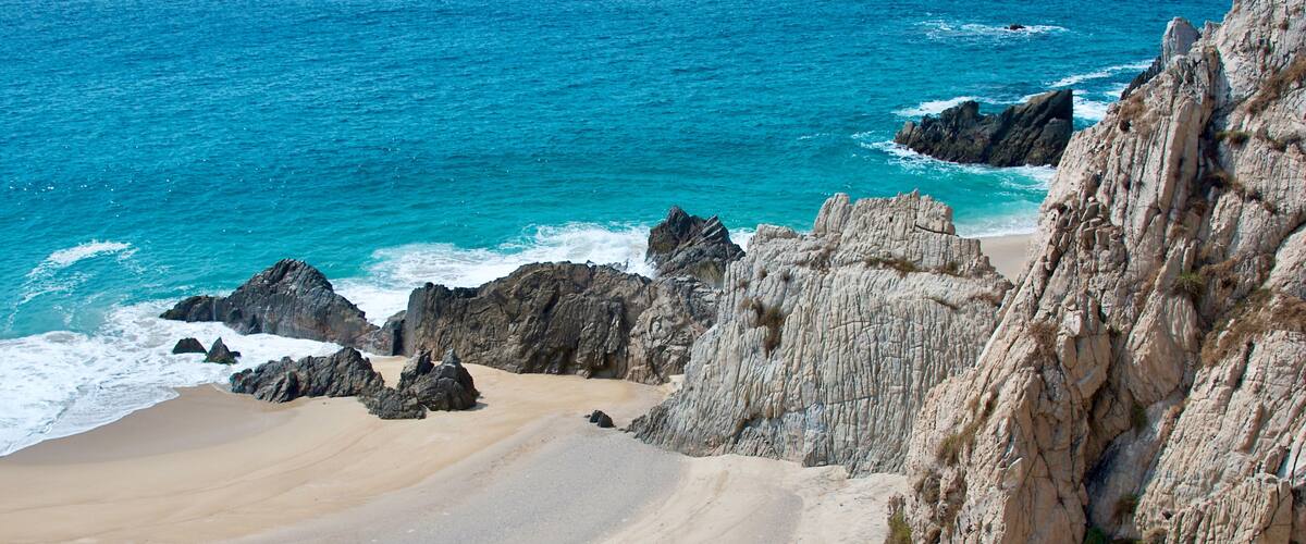 A coastal landscape with a sandy beach, rocky cliffs, and the ocean.