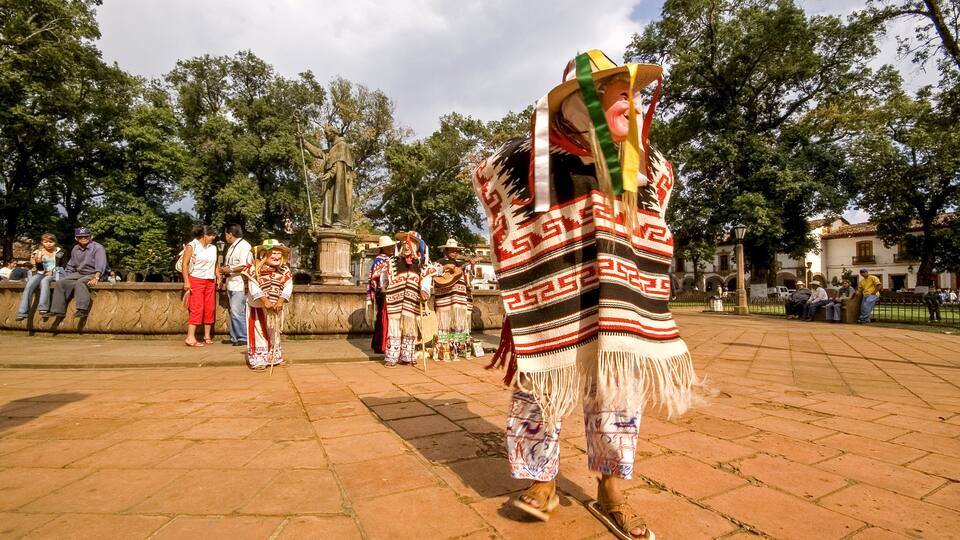 A person in traditional attire walking in a public square with a statue in the background.
