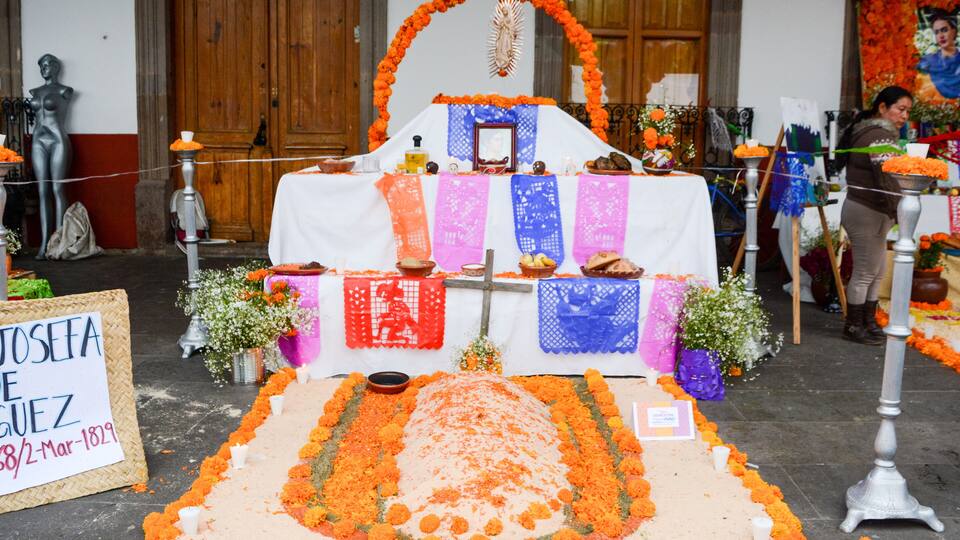A traditional altar with marigold flowers, a cross, and a sign reading "Josefa Guez 38/2-Mar-1829".
