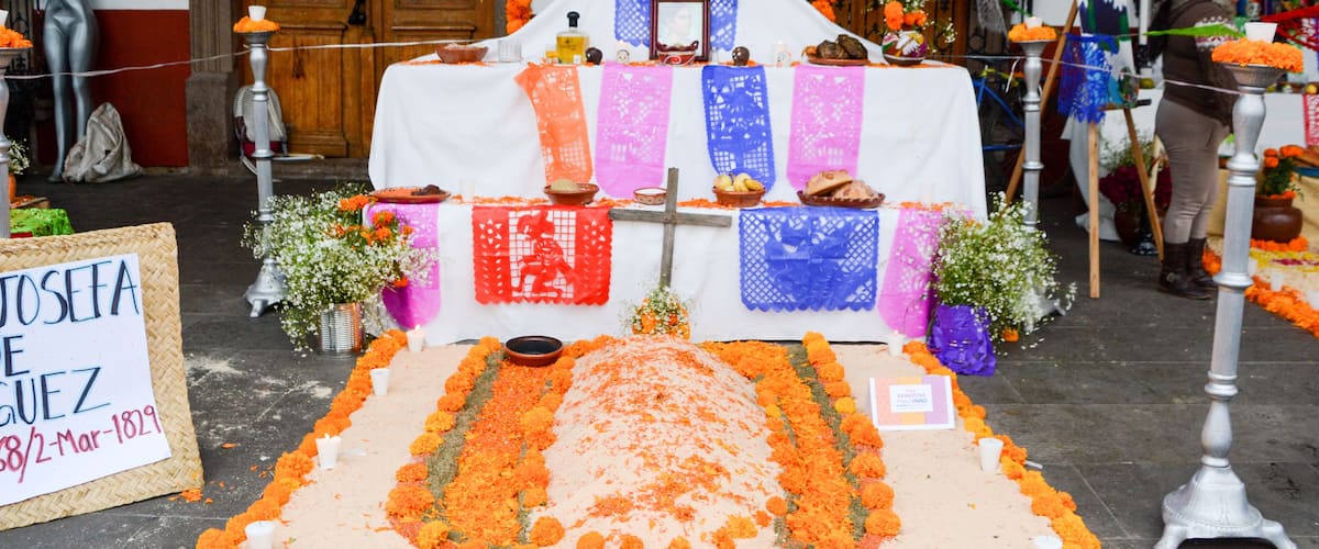 A traditional altar with marigold flowers, a cross, and a sign reading "Josefa Guez 38/2-Mar-1829".
