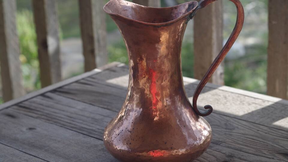 A copper pitcher on a wooden table.