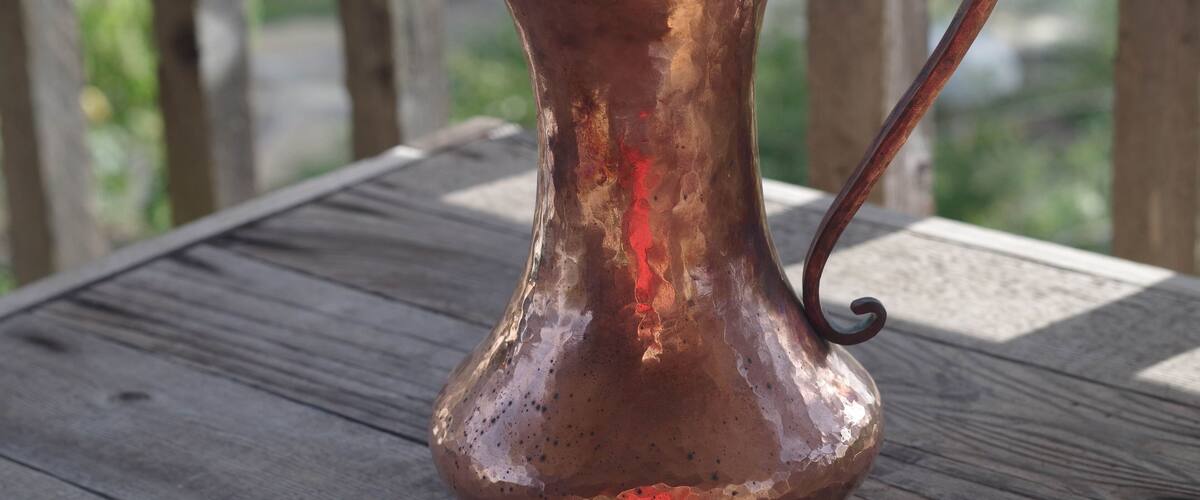 A copper pitcher on a wooden table.