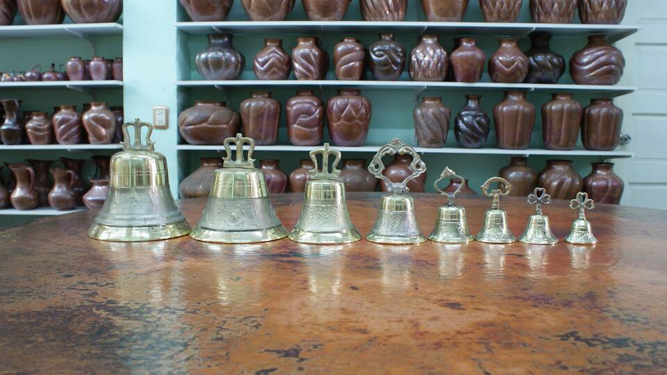 A display of various ceramic vases and metal bells on shelves and a table.