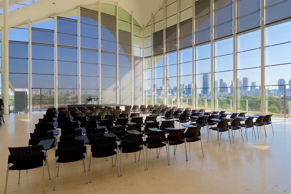A large indoor space with rows of chairs and tables, large windows, and a cityscape view.