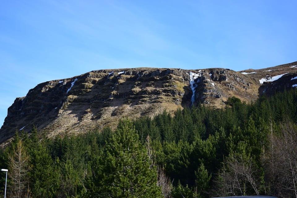 A mountain with a waterfall and dense forest.