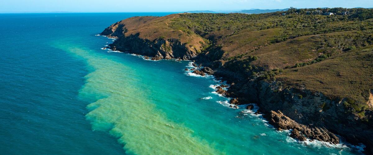 A coastal landscape with clear turquoise waters, rocky cliffs, and a distant view of a settlement.