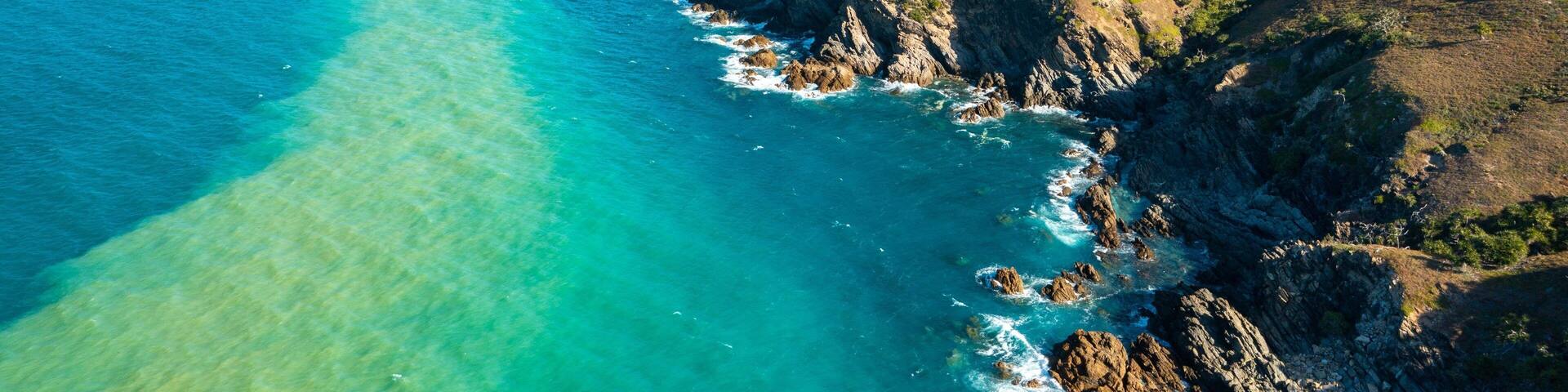 A coastal landscape with clear turquoise waters, rocky cliffs, and sparse vegetation.