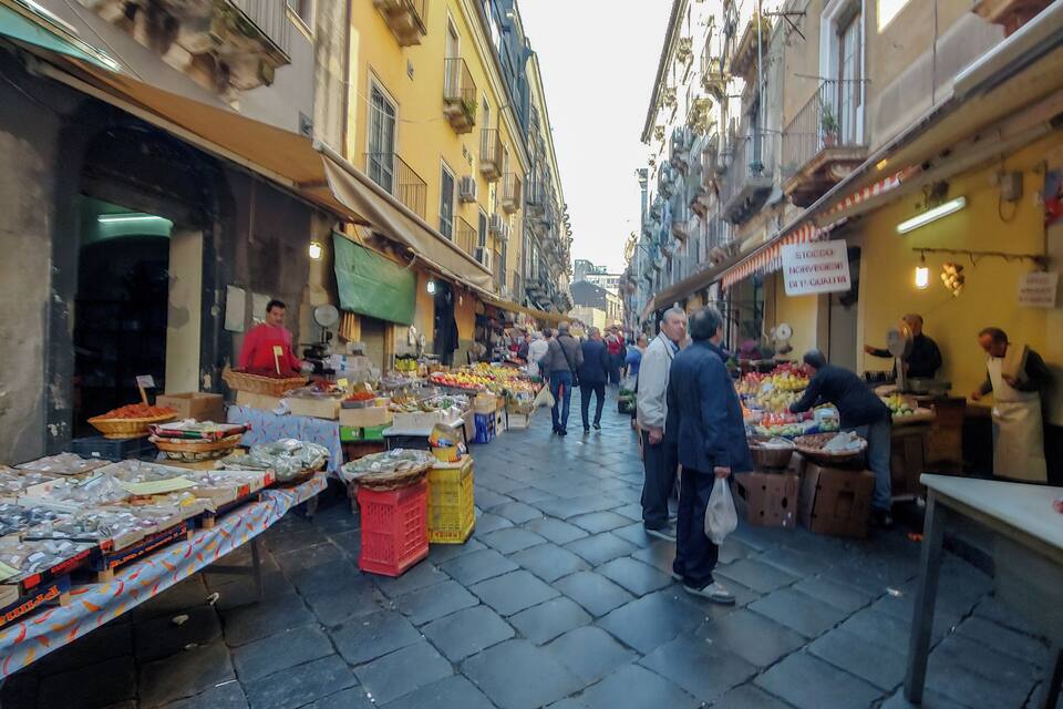 Un mercado al aire libre concurrido, con vendedores ofreciendo productos frescos y mercancías sobre mesas.