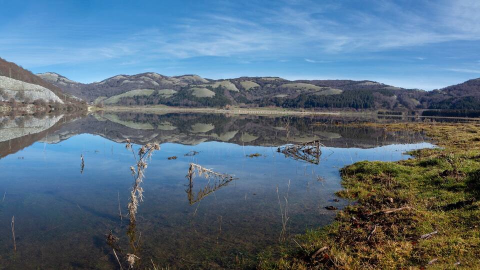 A serene lake with a clear reflection of a hill and a small building.