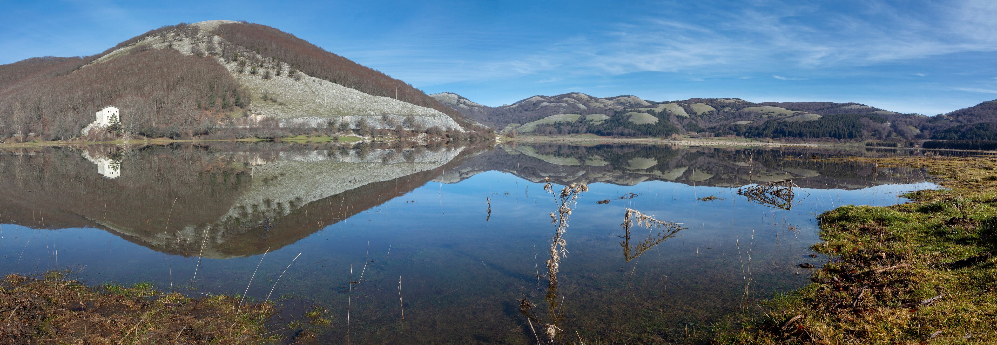 A serene lake with a clear reflection of a hill and a small building.