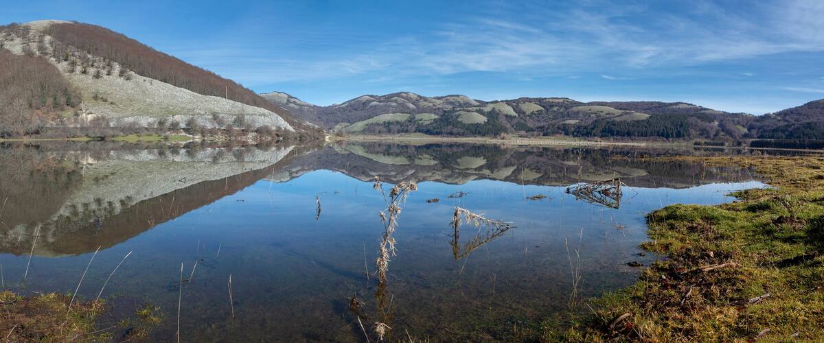 A serene lake with a clear reflection of a hill and a small building.