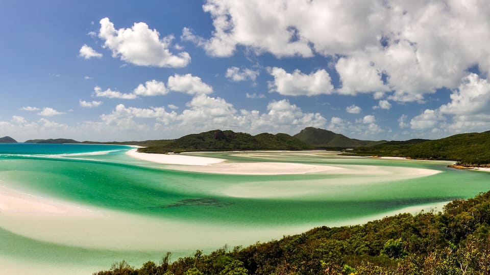 A coastal landscape with clear turquoise waters, white sandy beaches, and lush green hills.