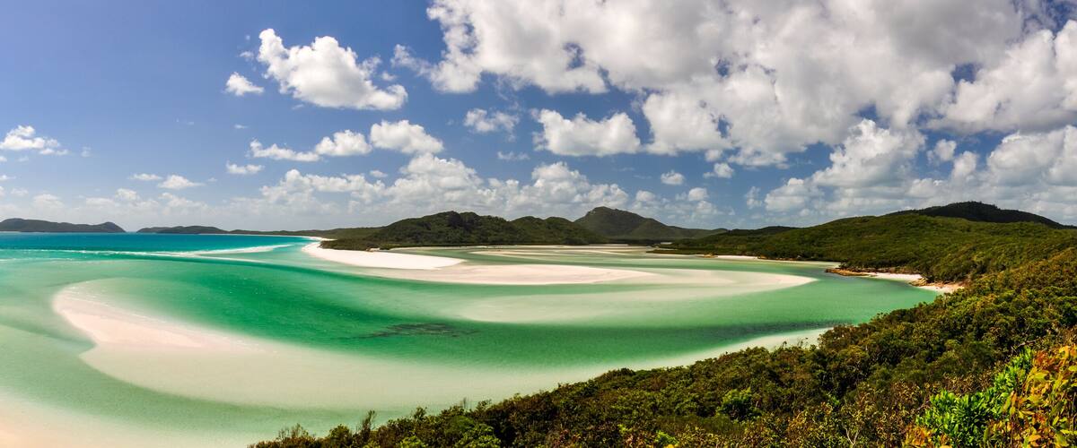 A coastal landscape with clear turquoise waters, white sandy beaches, and lush green hills.