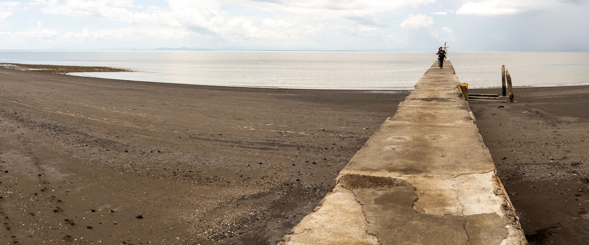 A concrete walkway leading to a beach with a person standing at the end.