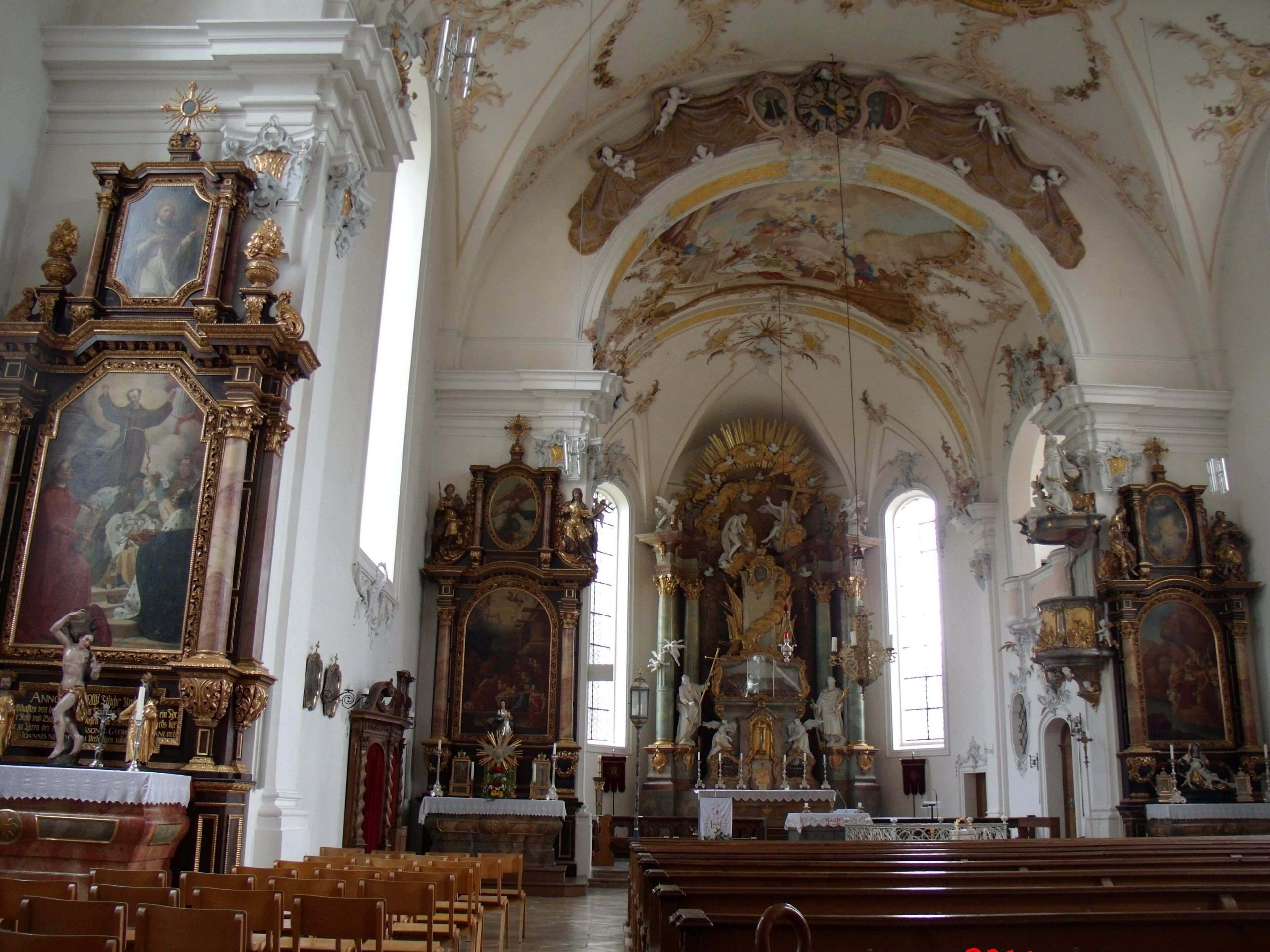An ornate church interior with elaborate altars, statues, and a high vaulted ceiling.