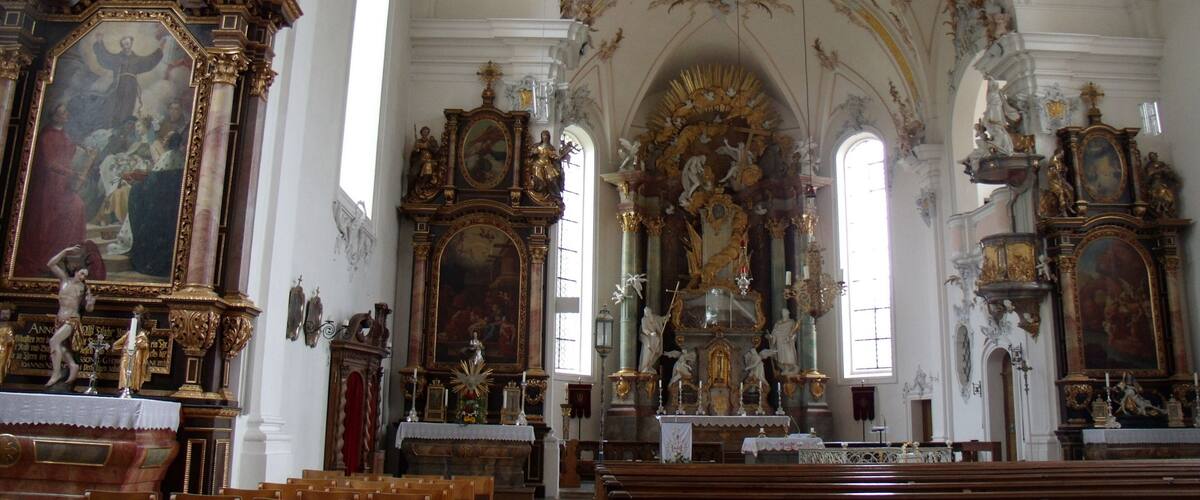 An ornate church interior with elaborate altars, statues, and a high vaulted ceiling.