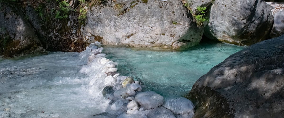 A clear stream flowing through a rocky gorge with large boulders and moss-covered rocks.