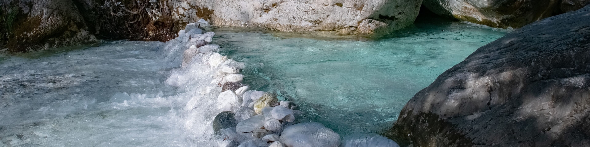 A clear stream flowing through a rocky gorge with large boulders and moss-covered rocks.