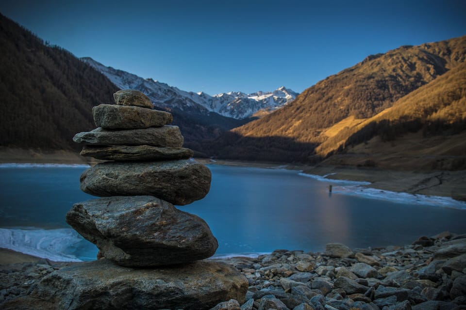Un ammasso di rocce accanto a un lago, con montagne sullo sfondo.