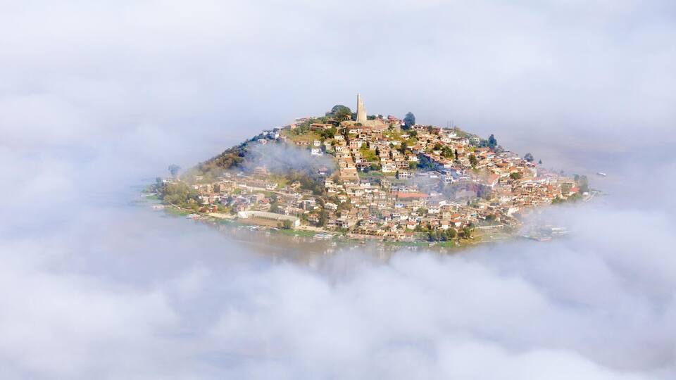 A town surrounded by clouds, with a prominent church on a hill.