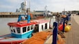 Um cais com um barco vermelho e azul chamado "HOLLADAYS" e redes de pesca laranja.