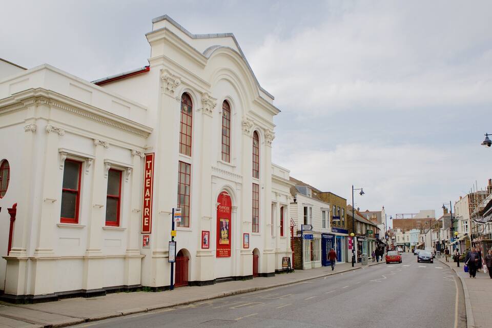 A street with a white building labeled "THEATRE" and a red sign.