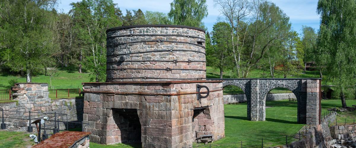 A stone structure with a cylindrical tower, a stone bridge, and a grassy area with trees.