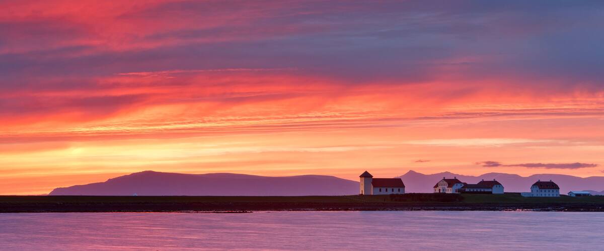 A sunset over a coastal landscape with houses and mountains in the background.